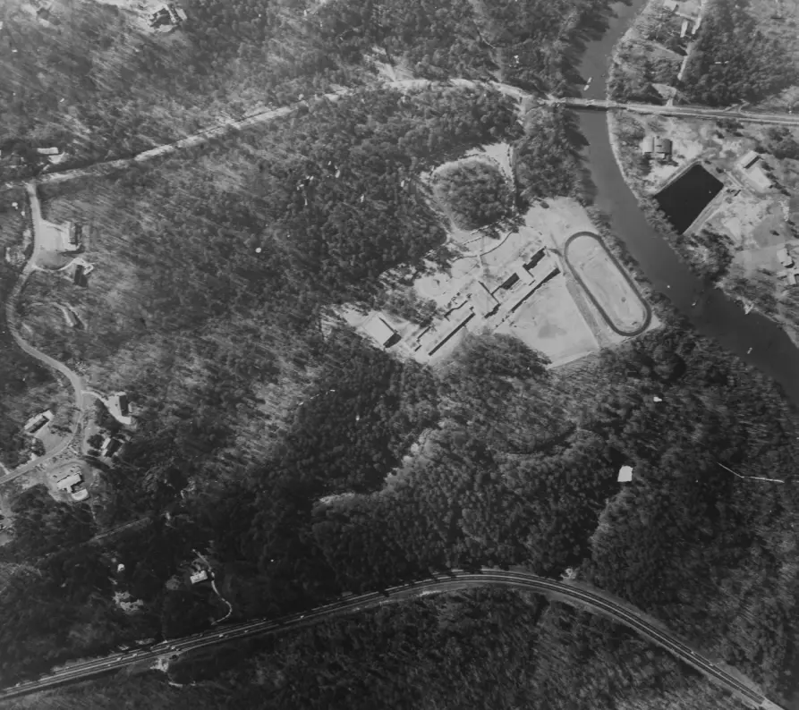 A black-and-white aerial photograph of The Lovett School's Paces Ferry Road campus, showing the central building, athletic track, and surrounding woodland.